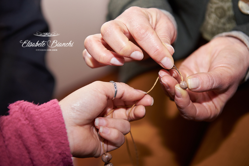 Mãos confeccionando um colar de contas, onde cada um coloca uma intenção ao bebê que vai nascer, em um chá de bênçãos em Caxias do Sul.