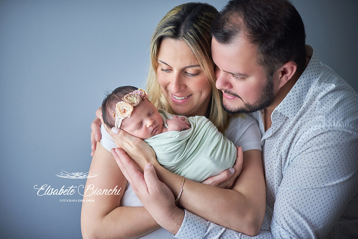 Pais dando colo à sua filha recém-nascida no ensaio newborn, em Caxias do Sul, RS.