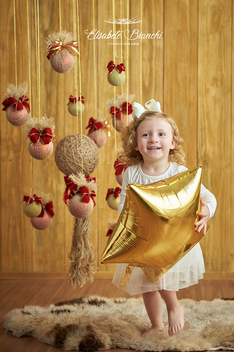 Menina brincando e sorrindo  com estrela dourada inflável, em ensaio de natal, em estúdio, Caxias do Sul - RS.