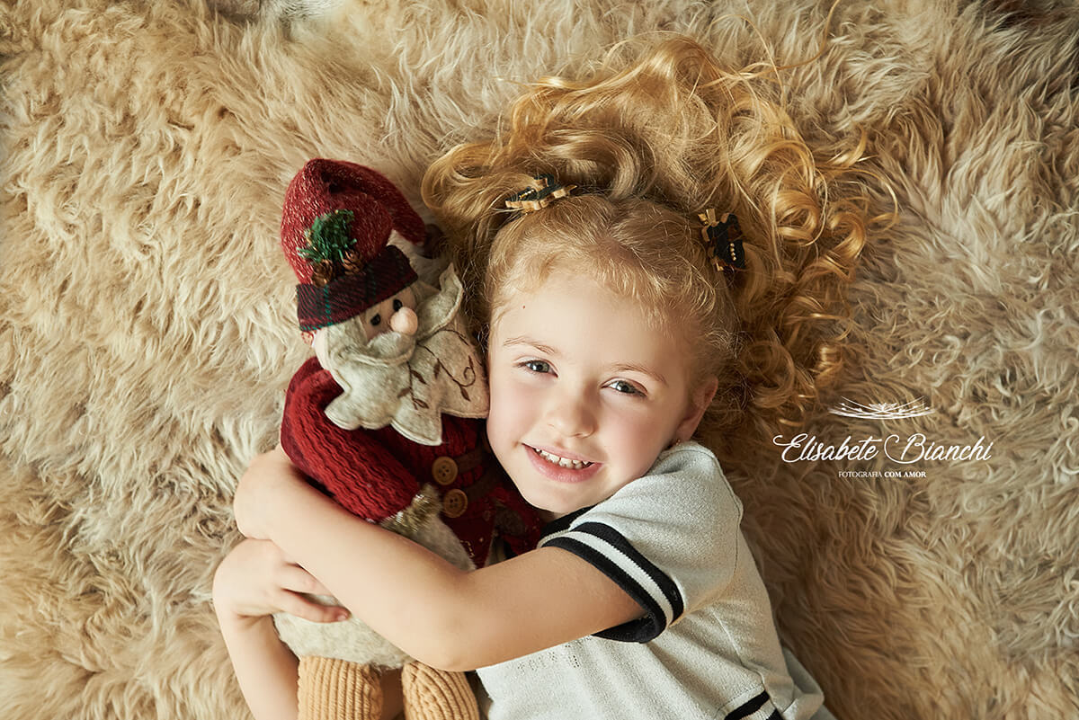 Menina deitada em pelego e abraçada em Papai Noel, em ensaio de natal, em estúdio, Caxias do Sul - RS.