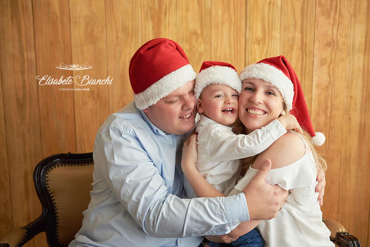 Família abraçada, de toucas de papai Noel, em mini-ensaio de natal 2018, em Caxias do Sul - RS>
