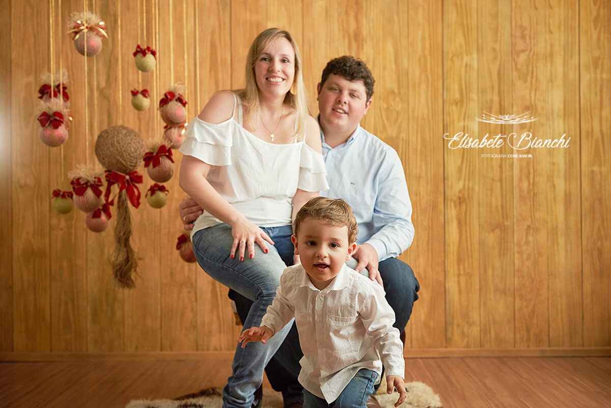 Pais sentados e criança a frente, em mini-ensaio de Natal 2018, Caxias do Sul - RS.