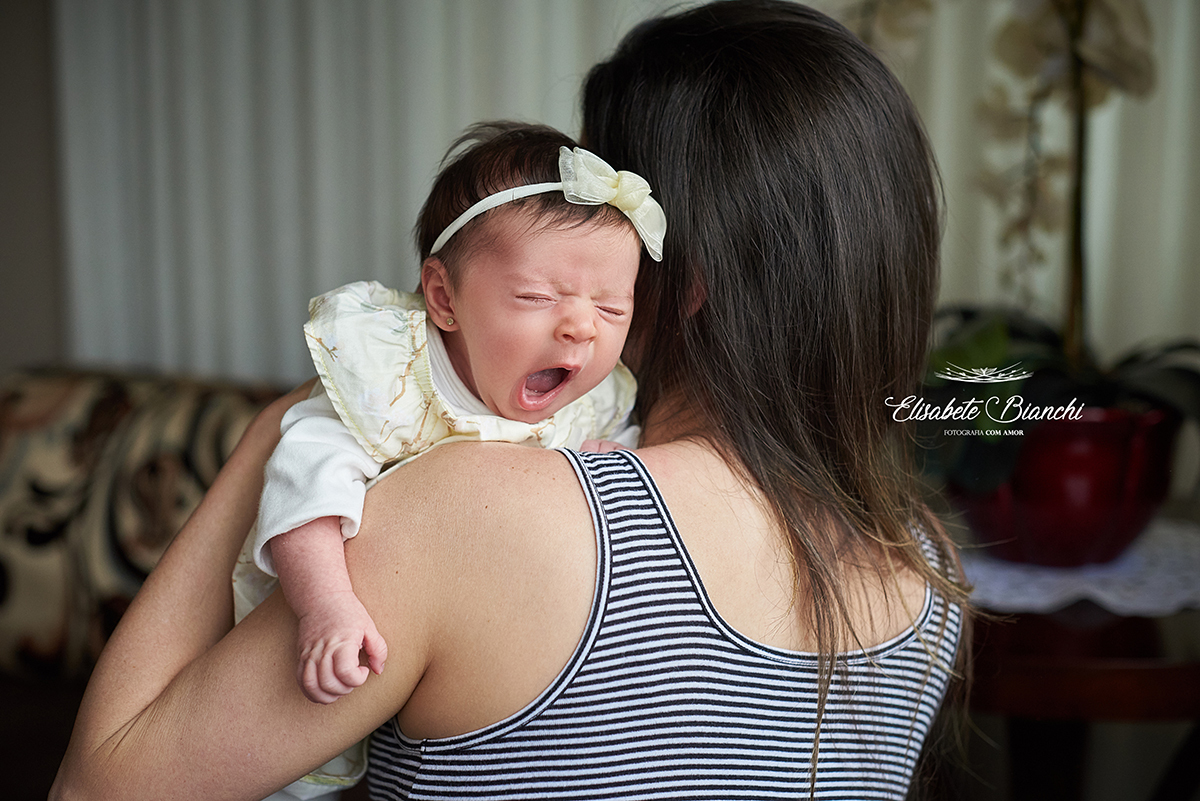 Bebê de 1 mês bocejando no colo da mãe, em pose de arroto, em ensaio de acompanhamento lifestyle, em Caxias do Sul, RS.