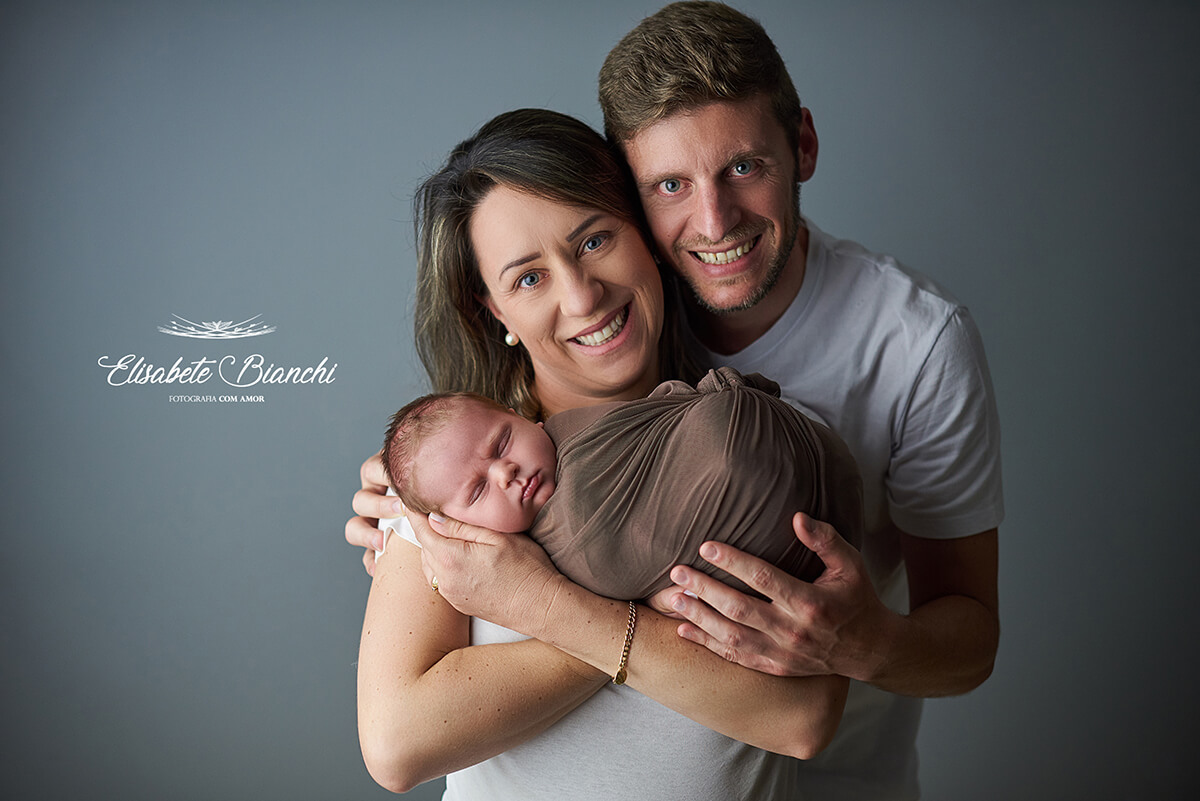 Pais felizes segurando no colo filho recém-nascido, em ensaio newborn em Caxias do Sul - RS.