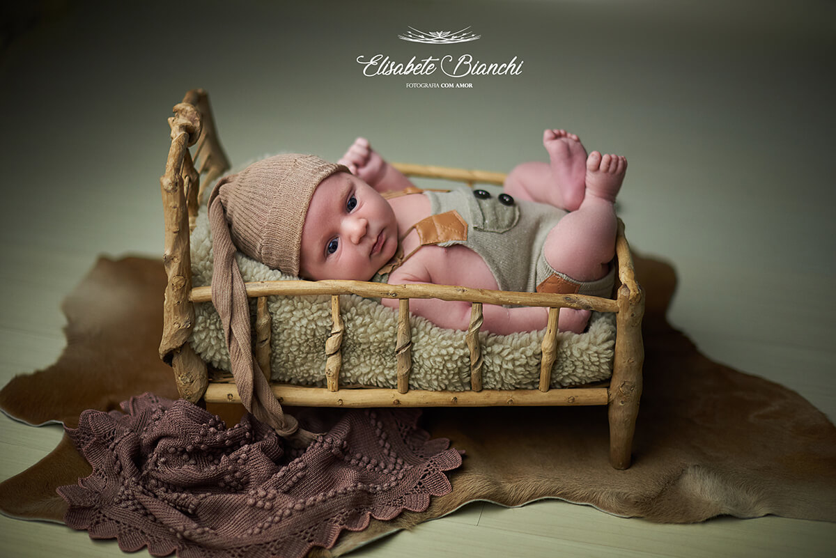 Bebê recém-nascido acordado, visto de lado, no prop caminha, em ensaio newborn em Caxias do Sul - RS.
