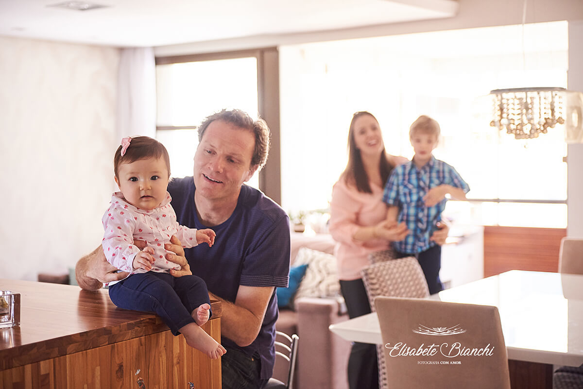Pai com filha de 7 meses e mãe com o filho mais velho, na sala de estar, em ensaio lifestyle na residência da família, em Caxias do Sul - RS.