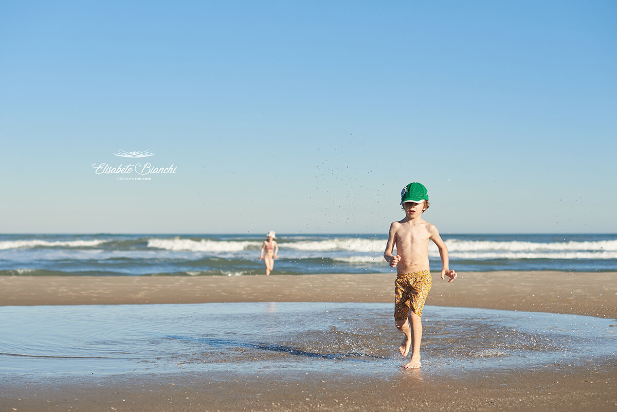 Menino saindo do mar a frente e menina atras, no mar de Bella Torres, Santa Catarina.