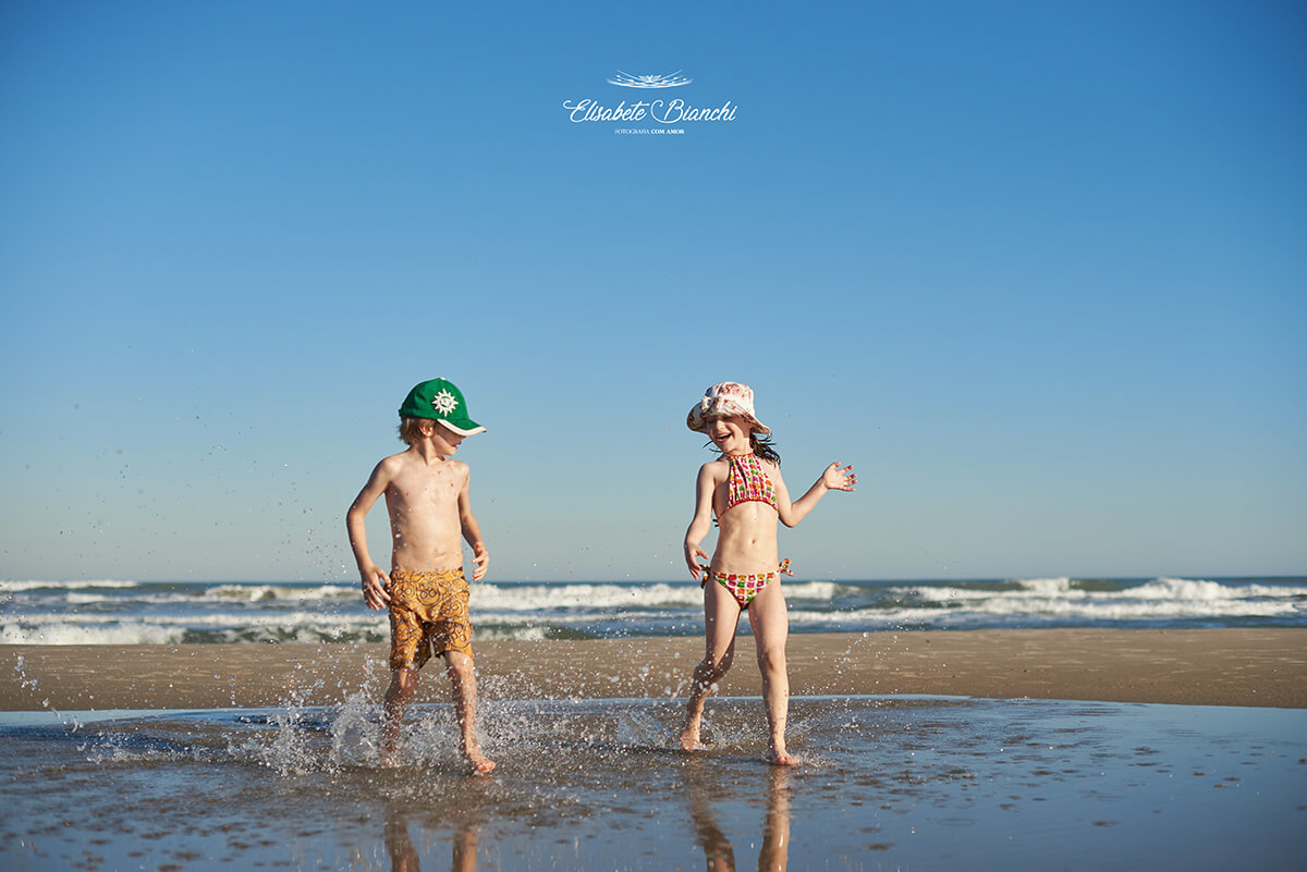 Crianças batendo o pé na água, no mar, em Bella Torres, Santa Catarina.