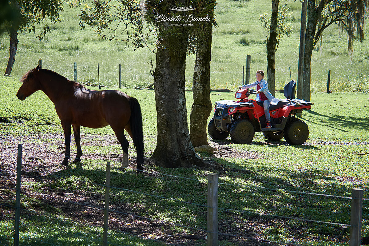 Menino em quadriciclo, em meio aos cavalos, em Fazenda Souza, no ensaio fotográfico externo 
 em Caxias do Sul.