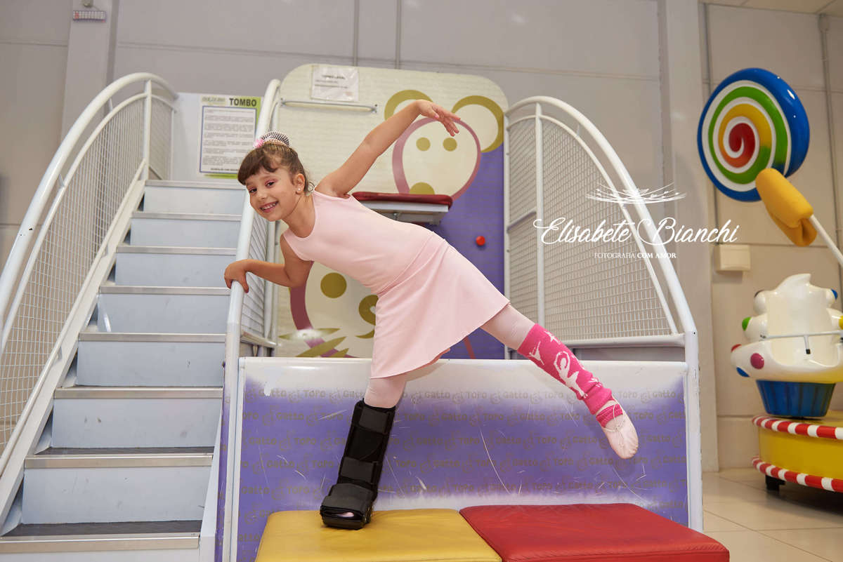 Aniversariante brincando na sua festa de aniversário, com tala em uma perna, em pose de bailarina, na casa de festas Gato & Topo, em Caxias do Sul - RS.