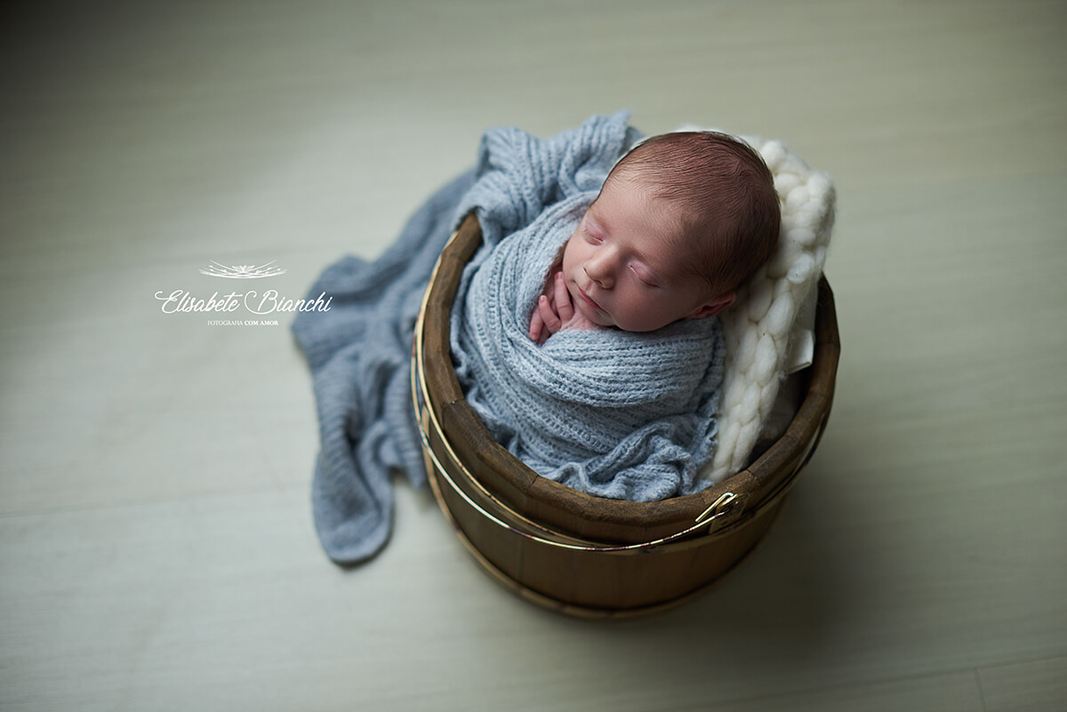 Bebê recém-nascido enrolado em mantinha, dentro de balde, no ensaio Newborn, em Caxias do Sul - RS
