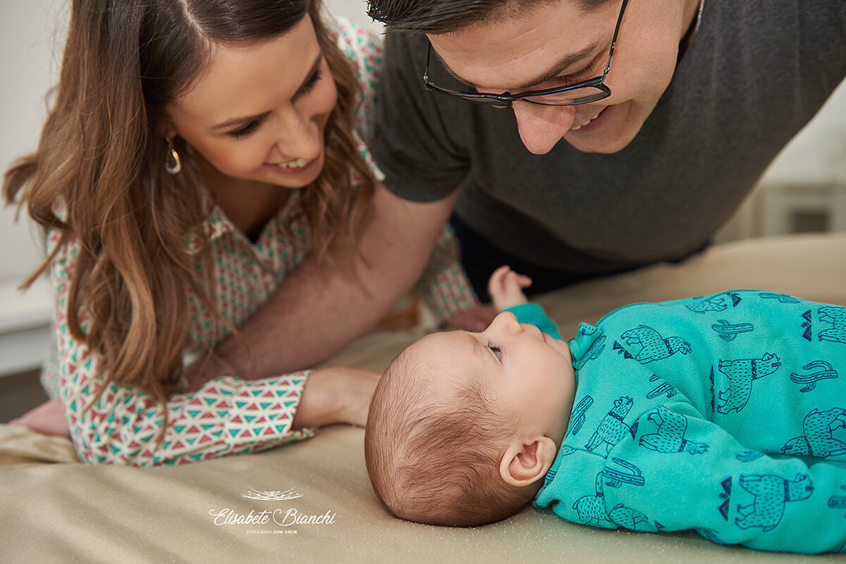Mamãe e papai olhando e conversando com seu bebê de 3 meses, em ensaio lifestyle de acompanhamento, em São Marcos, RS.