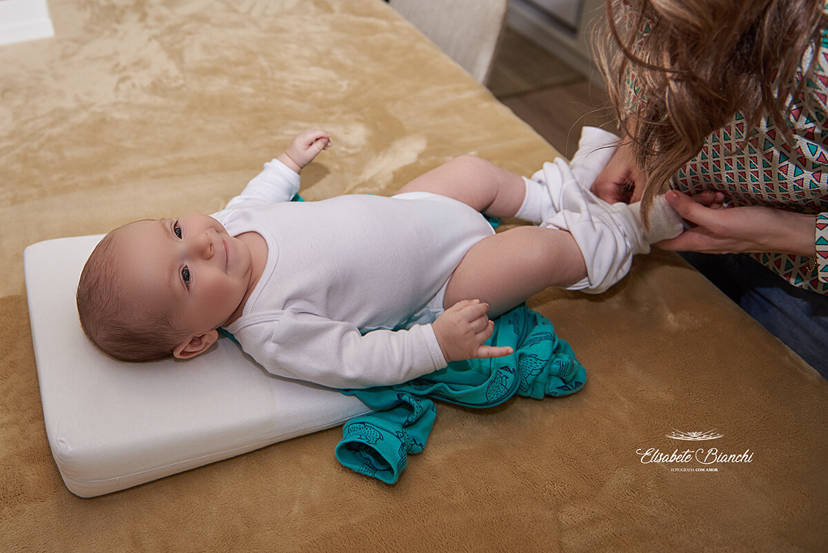Bebê de 3 meses sorrindo, e mamãe lhe vestindo, em ensaio lifestyle de acompanhamento, em São Marcos, RS.