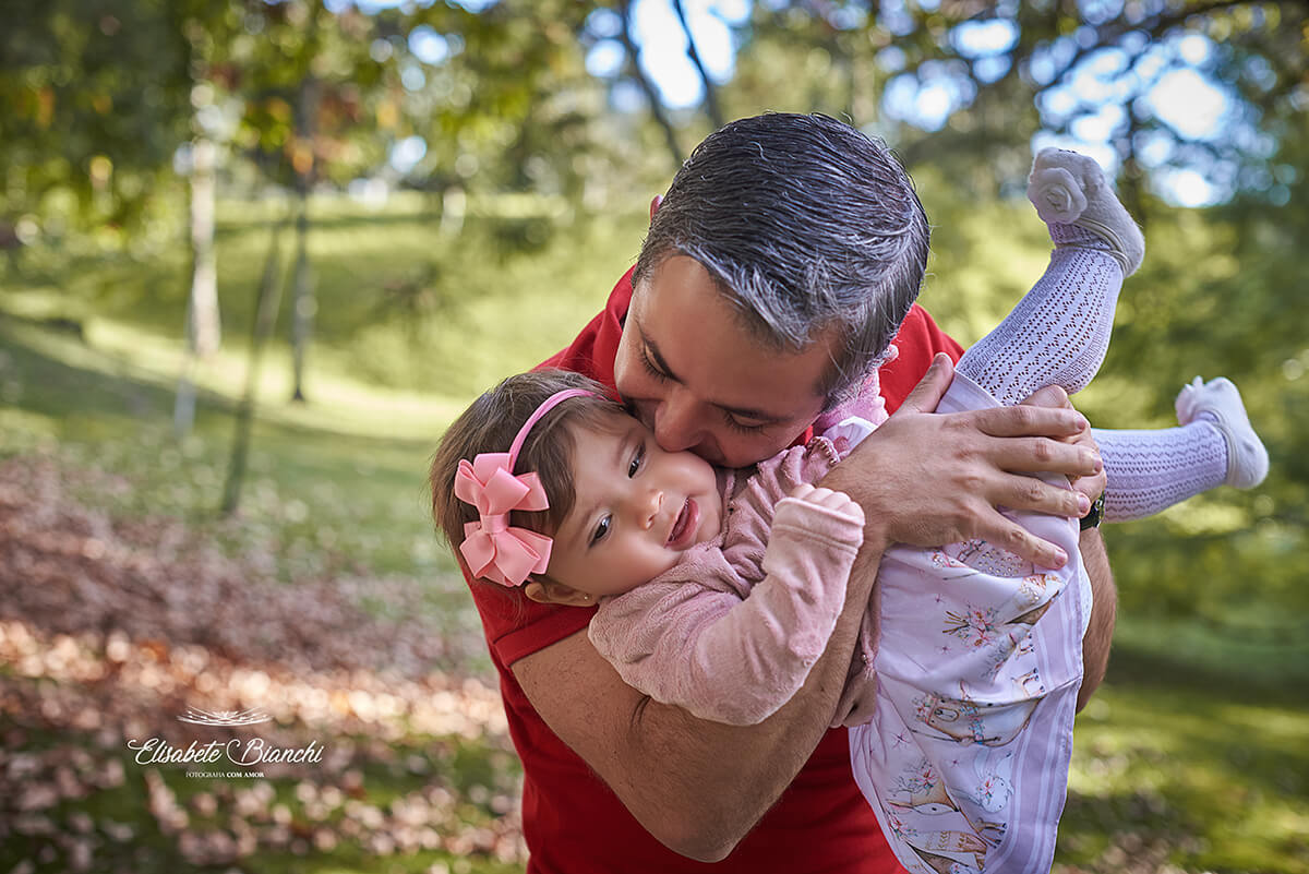 Pai brincando e beijando filha de 8 meses, em acompanhamento fotográfico, em Caxias do Sul - RS.
