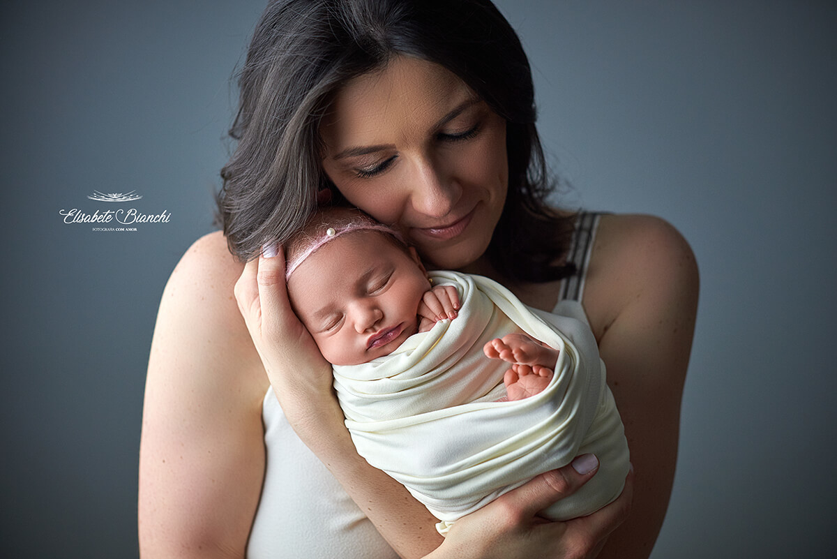 Mãe segurando sua bebê recém-nascida e encostando seu rosto nela, em ensaio newborn, Caxias do Sul - RS