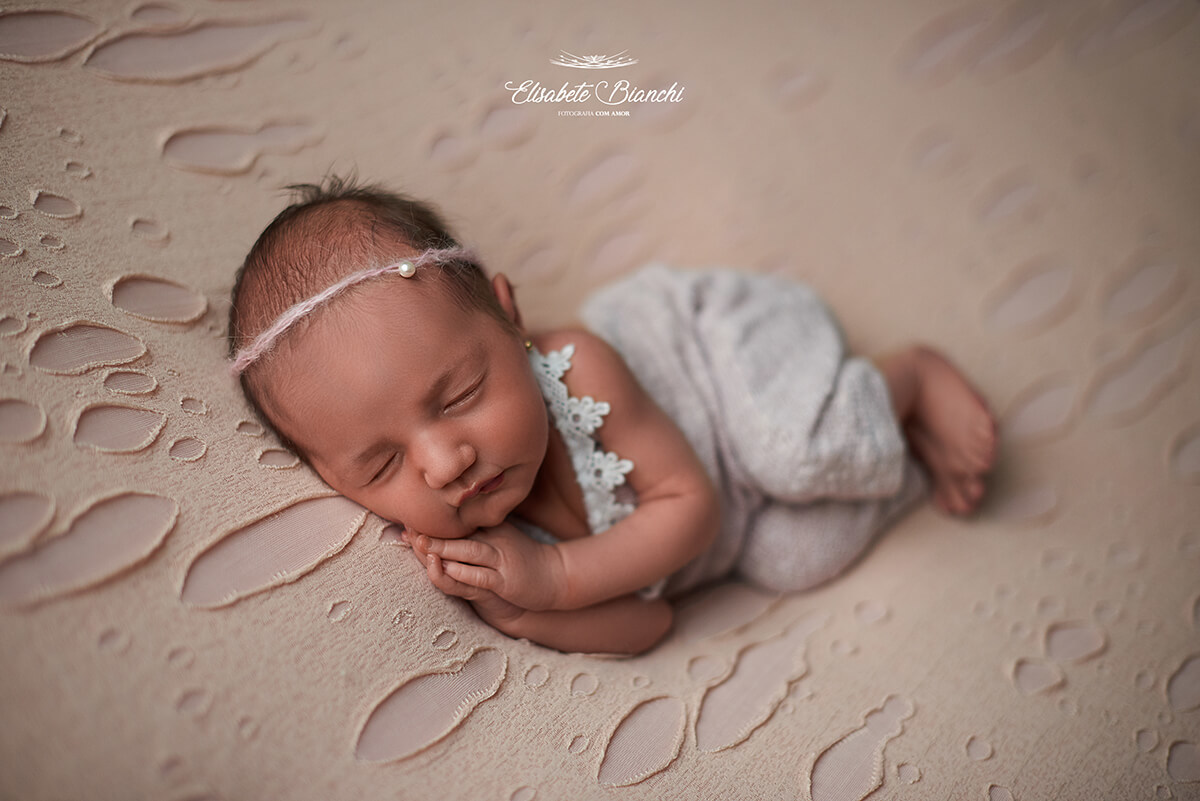 Bebê recém-nascida deitada de lado, com as mãos em oração, abaixo da bochecha, em ensaio newborn, Caxias do Sul - RS