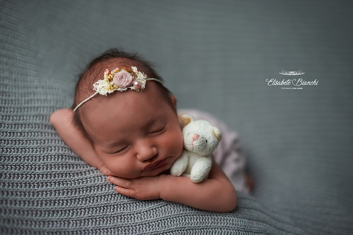 Bebê recém-nascida de barriga para baixo, apoiando a cabeça sobre os braços, e abraçada com um bichinho de pelúcia, em ensaio newborn, Caxias do Sul - RS