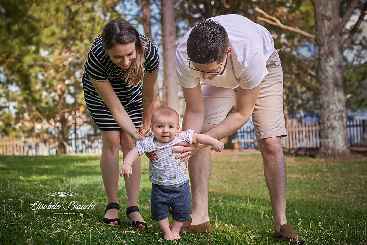 Família em um parque, ajudando o bebê de 6 meses a caminhar.