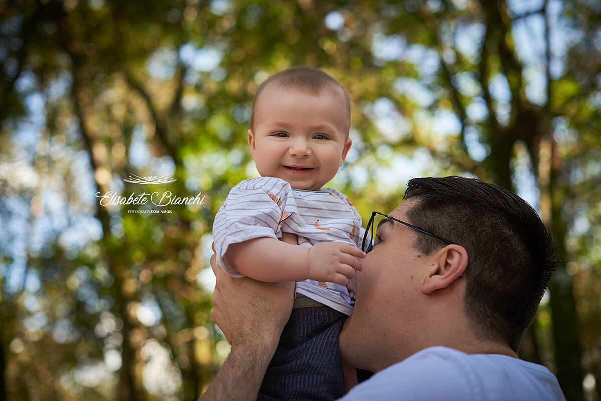 Pai fazendo cócegas, com a boca, na barriga do bebê de 6 meses de idade, fazendo ele rir.