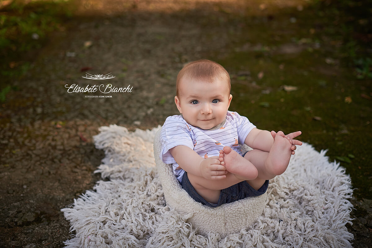 Bebê sorrindo, sentado em uma poltrona, erguendo os pés e segurando-os.