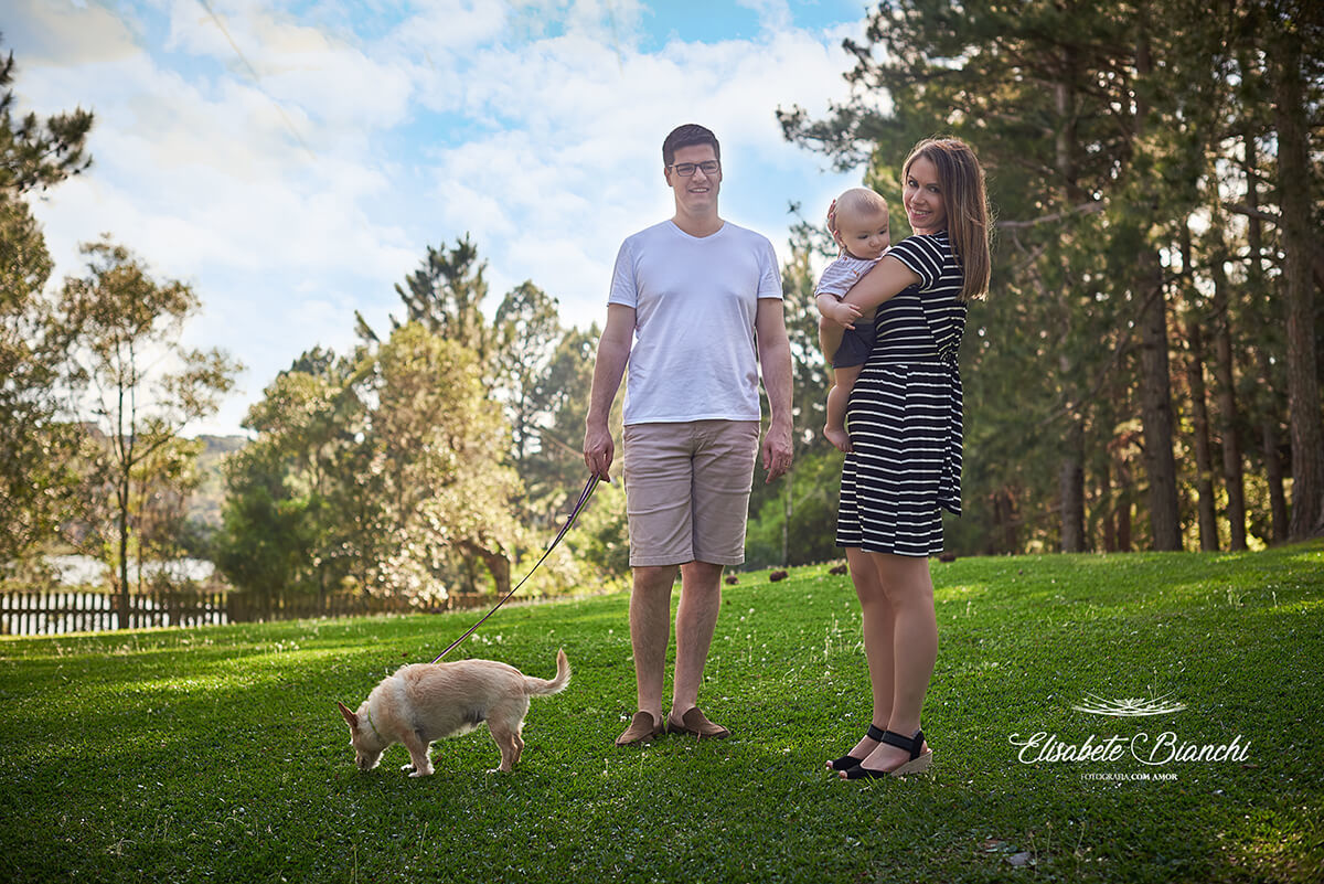Família em um parque, mãe com bebê de 6 meses no colo e cão na coleira.