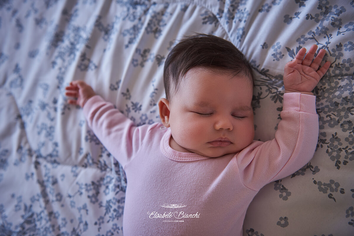 Bebê de 1 mês dormindo na capa nos pais, com os braços para cima, em ensaio lifestyle na residência dos pais, em Caxias do Sul - RS.