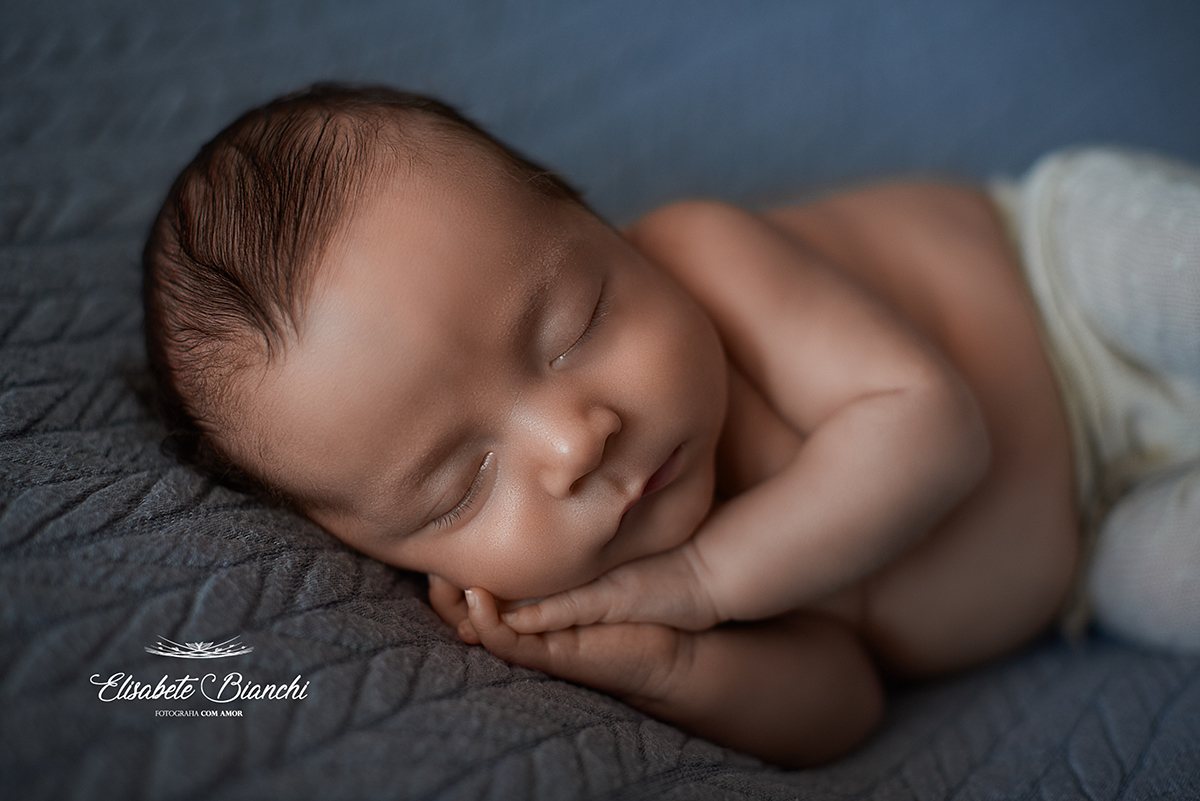 Bebê nascido prematuro, dormindo de lado, com as mãos palma com palma debaixo do rosto, em ensaio newborn.