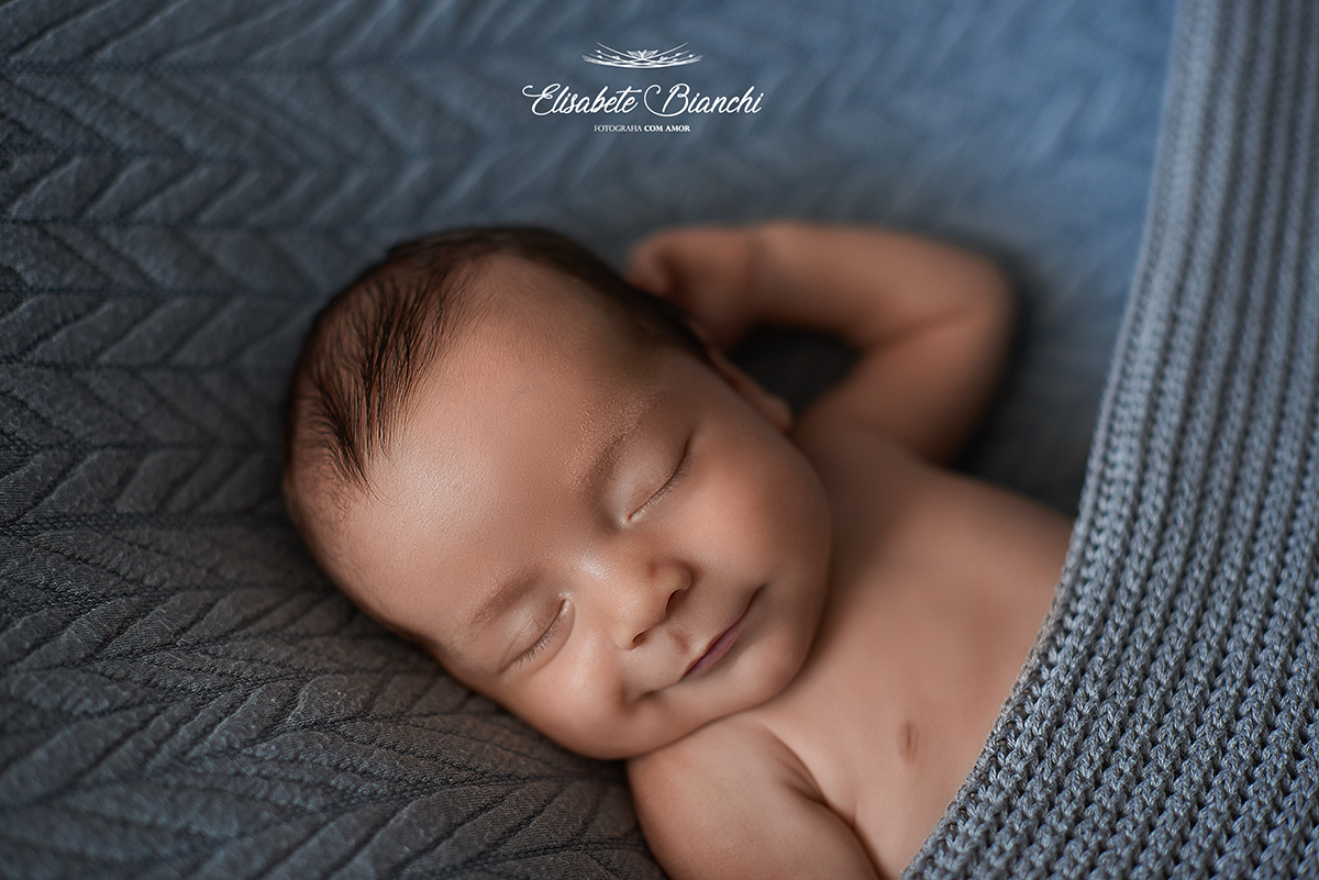 Bebê sorrindo, dormindo debaixo da coberta, em ensaio newborn