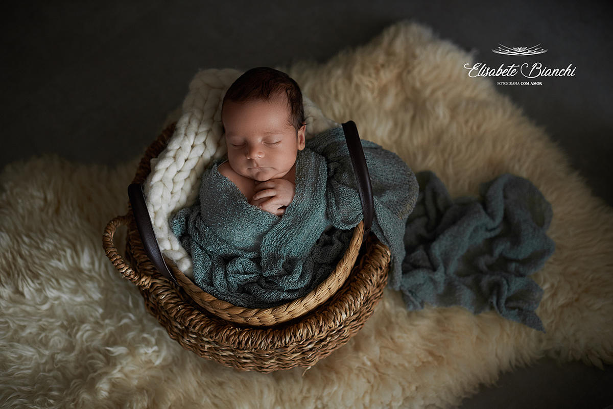 Bebê dentro de um cesto, enrolado em um tecido, em ensaio newborn.