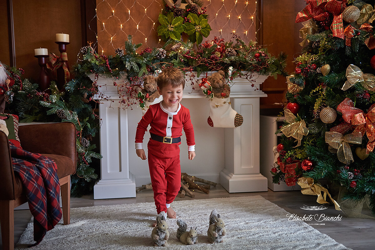 Menino vestido de papai noel, correndo pela sala decorada de natal, em Caxias do Sul, RS.