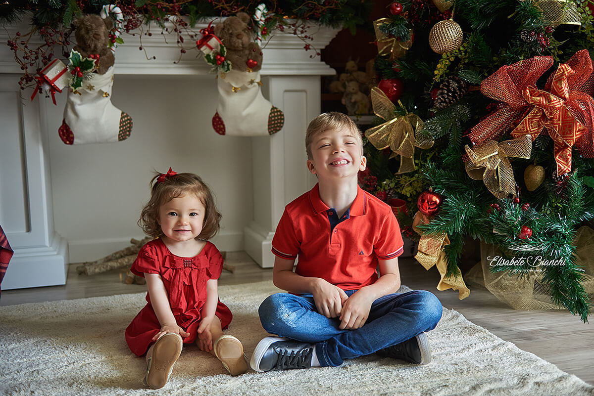 Irmãos sentados no tapete da sala decorada para o natal, em Caxias do Sul.