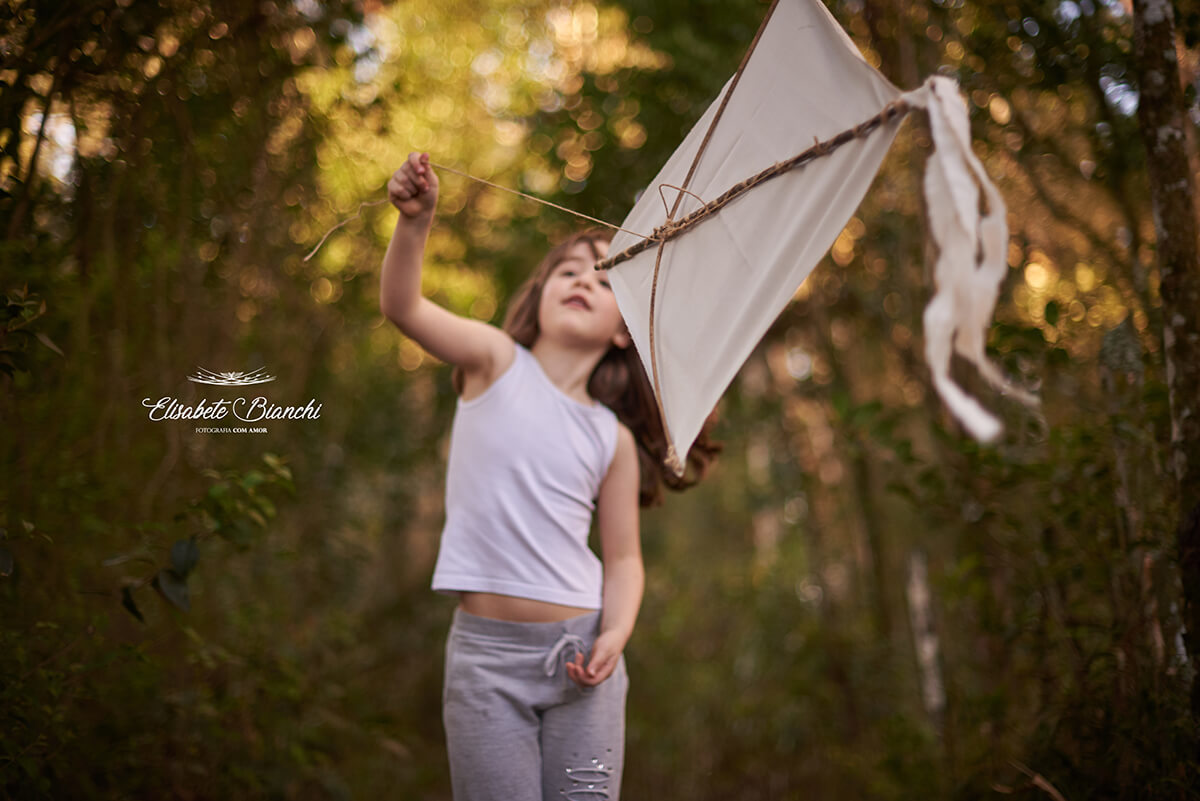 Menina brincando com uma pandorga. A pandorga está em foco e a menina não. 