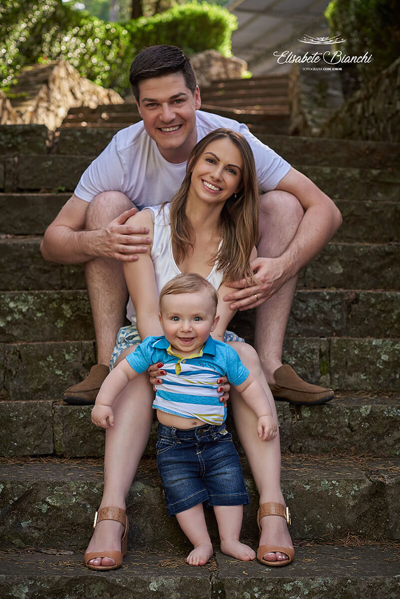 Família sentada na escadaria. Bebê de 9 meses embaixo, mãe no meio e pai acima.