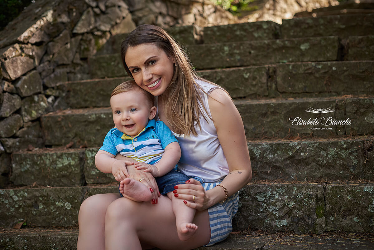 Mãe segura seu bebê de 9 meses no colo, sentada em uma escadaria.