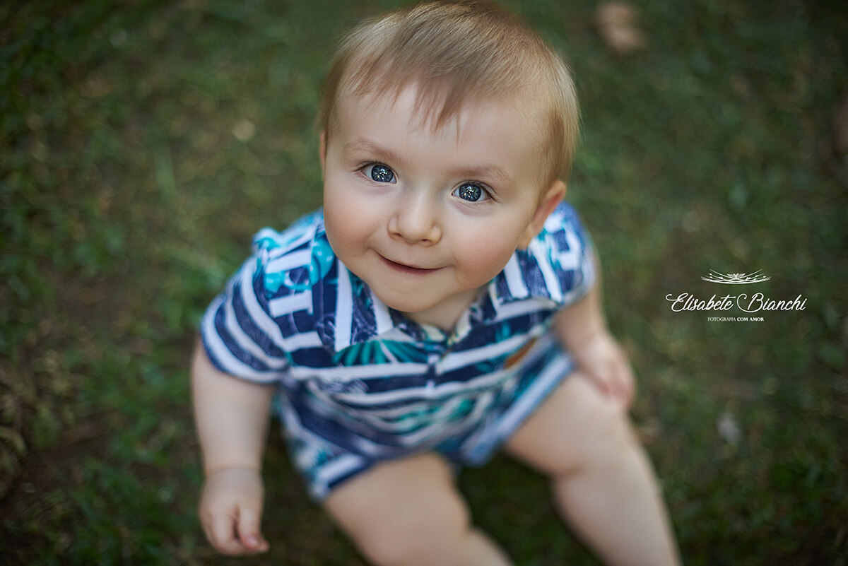 Bebê de 9 meses sorrindo e sentado, visto de cima.