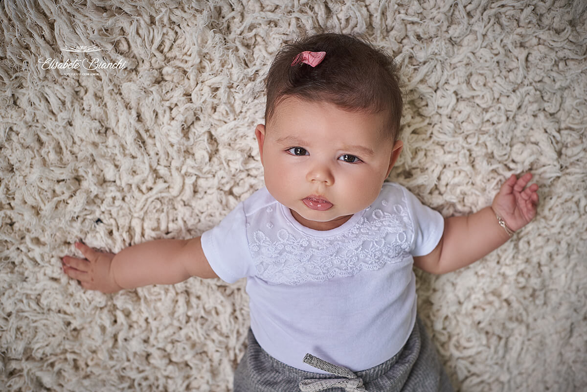 Bebê de 4 meses deitada em um tapete cor cru,  em Ana Rech, Caxias do Sul.