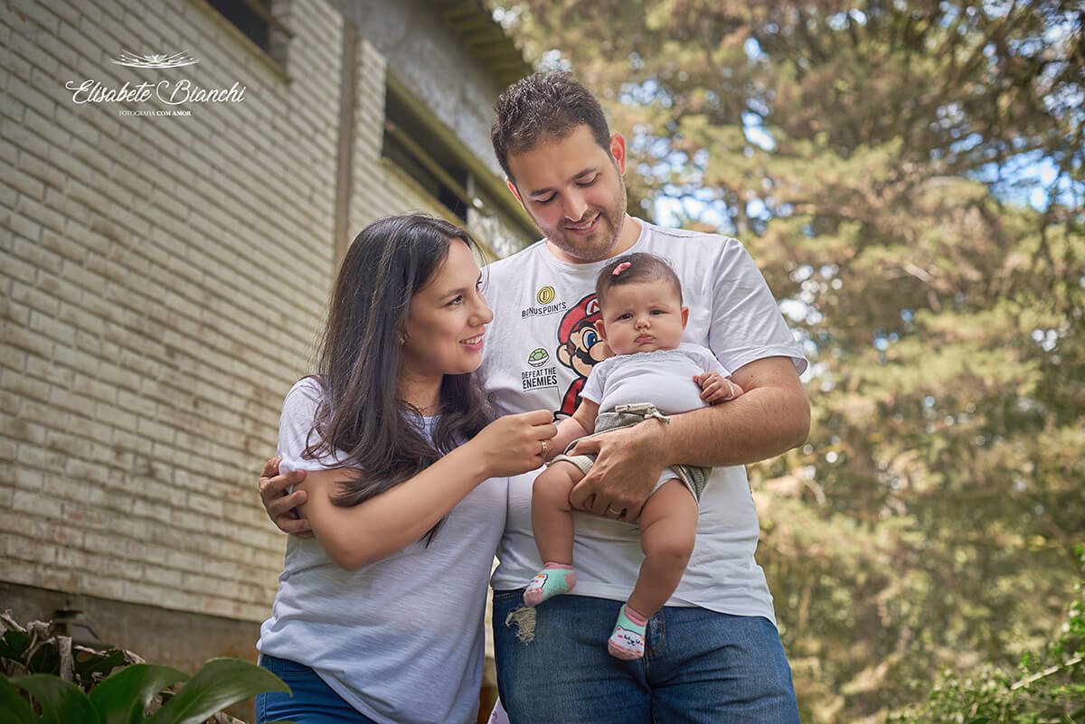 Família, em pé, com sua bebê de 4 meses no colo, virada para frente e os pais a olhando, em Ana Rech, Caxias do Sul.