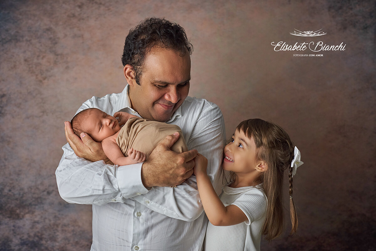 Pai com seu bebê recém-nascido no colo e sua filha mais velha ao lado, no ensaio newborn, em Caxias do Sul.