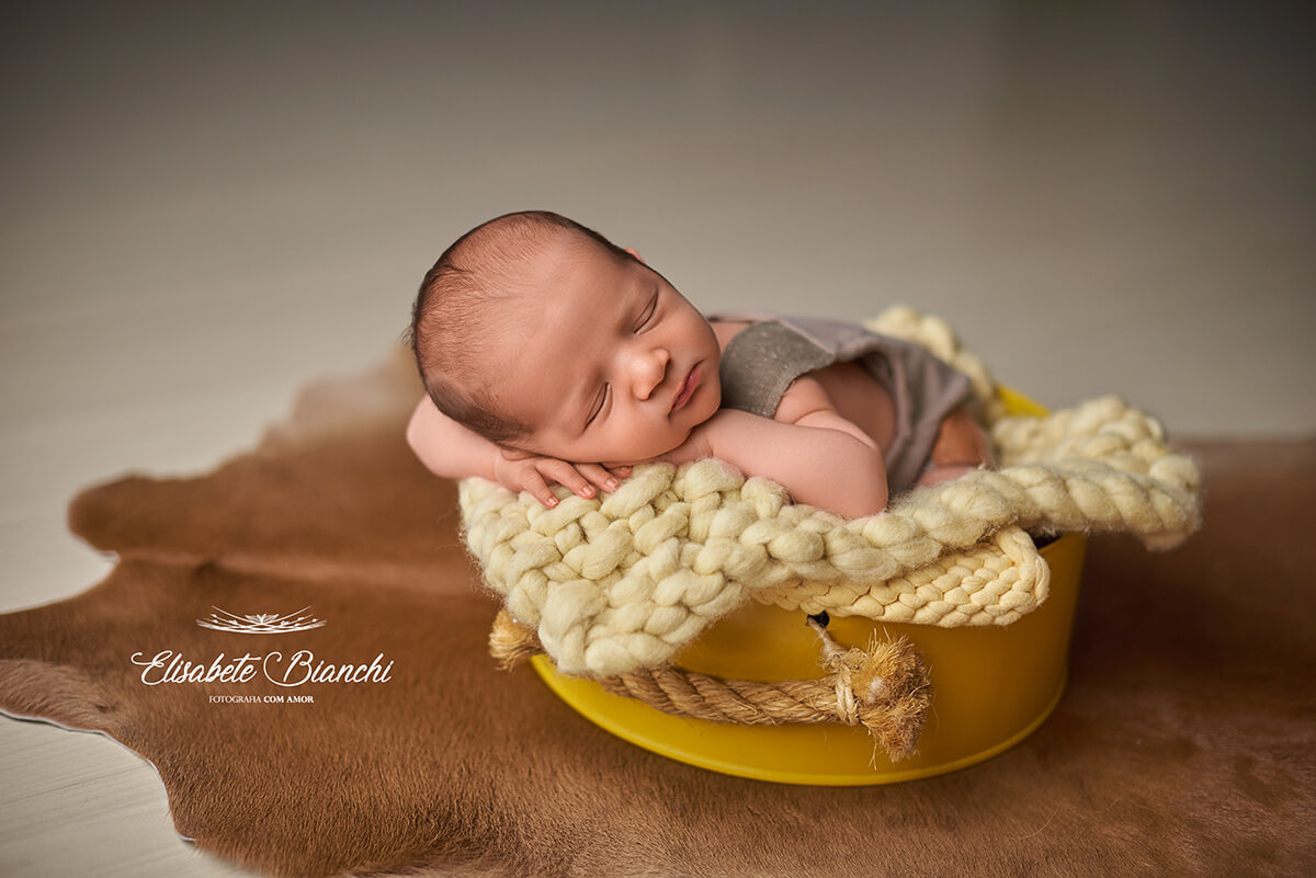 Bebê recém-nascido dormindo  dentro de um cestinho amarelo, no ensaio newborn, em Caxias do Sul.