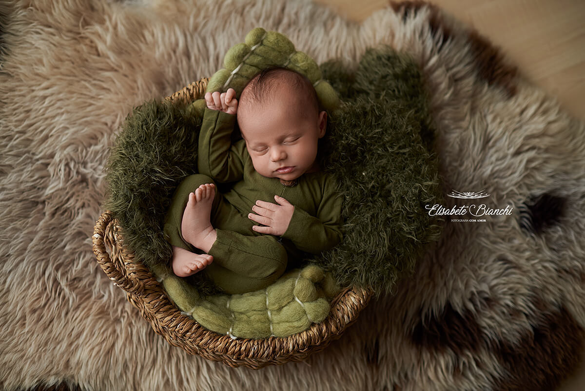 Bebê recém-nascido dormindo em um cestinho, de barriga para cima, em ensaio newborn, Vacaria, RS.