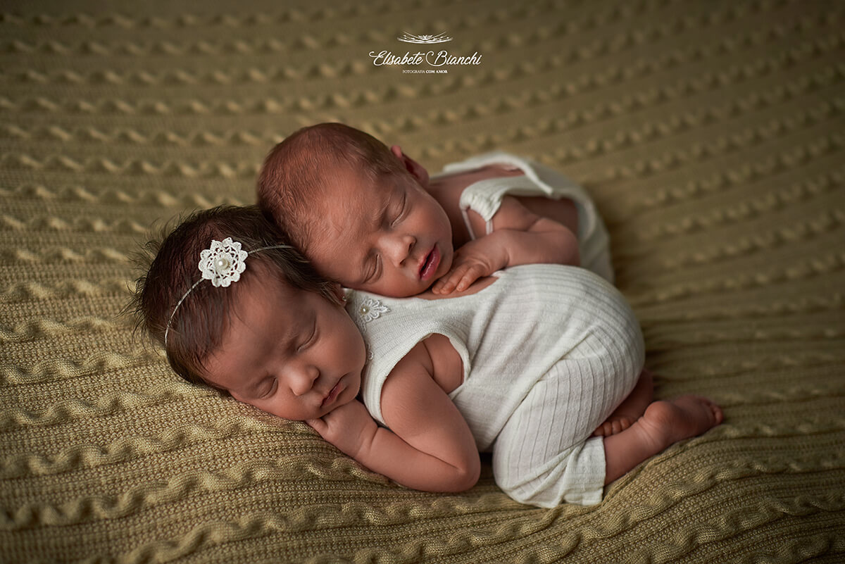 Casal de gêmeos dormindo deitados um sobre o outro, de barriga para baixo, em ensaio newborn, em Caxias do Sul.