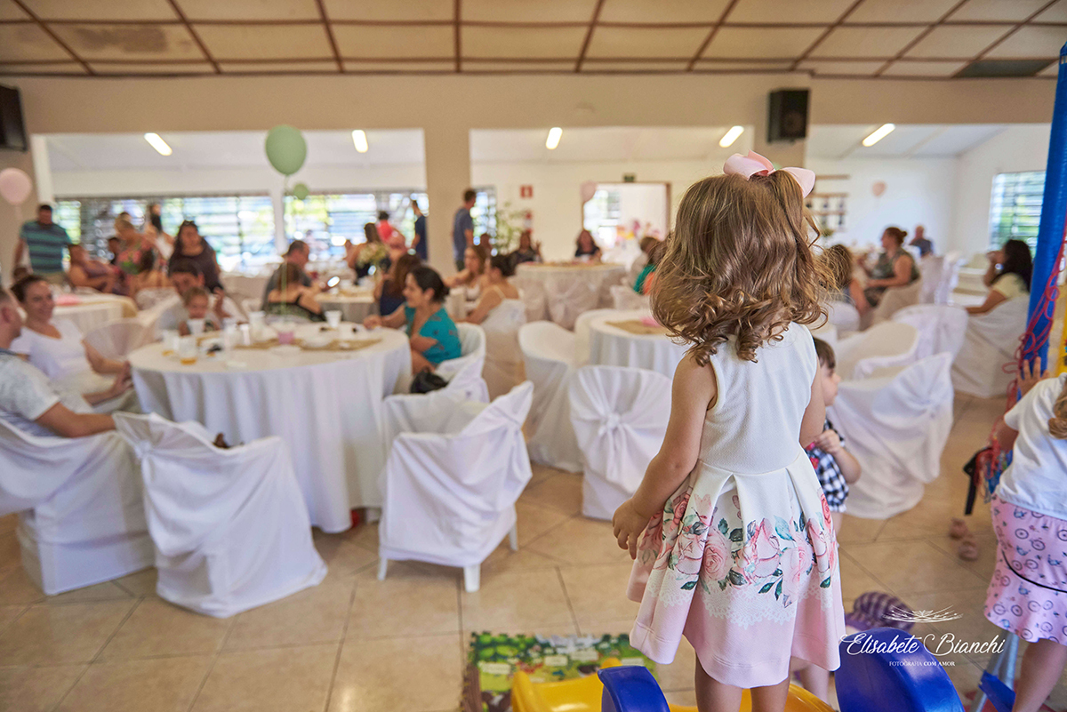 Aniversariante, em cima de um brinquedo, observando os convidados de sua festa de 2 anos de idade, na ACOMAC, em Caxias do Sul.