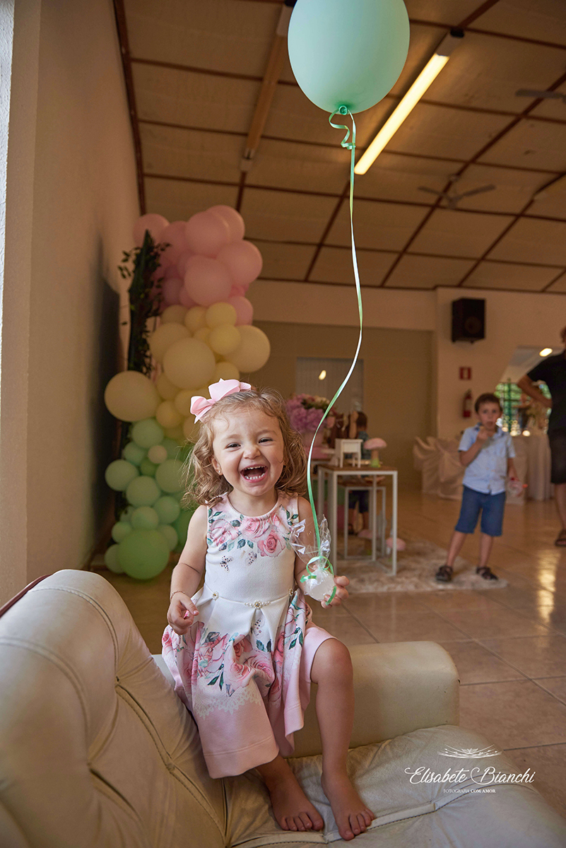 Aniversariante rindo e brincando com um balão com gás hélio, em sua festa de 2 anos de idade, em Caxias do Sul.
