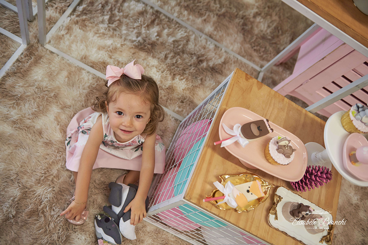 Menina sentada no chão, vista de cima para baixo, ao lado da mesa principal de aniversário de 2 anos, em Caxias do Sul.