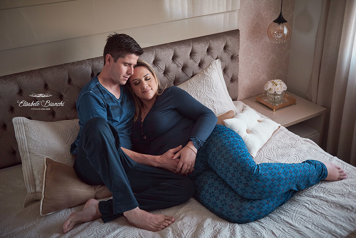 Casal gestante em tempo de pandemia, deitado de pijama na cama de sua casa, em ensaio fotográfico na residência, em Caxias do Sul.
