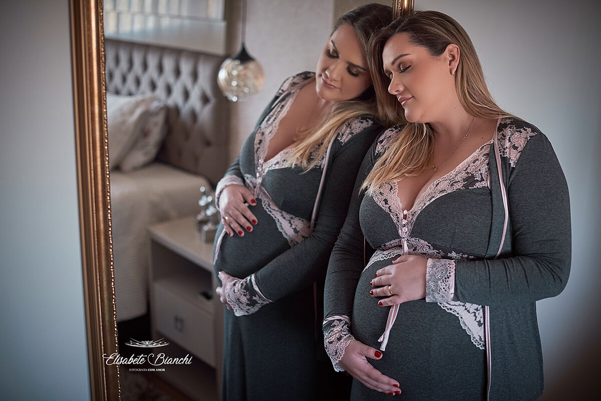 Gestante de olhos fechados, vestindo camisola, duplicada pelo reflexo do espelho em que está escorada, no seu quarto, em tempos de pandemia, em ensaio fotográfico em Caxias do Sul.