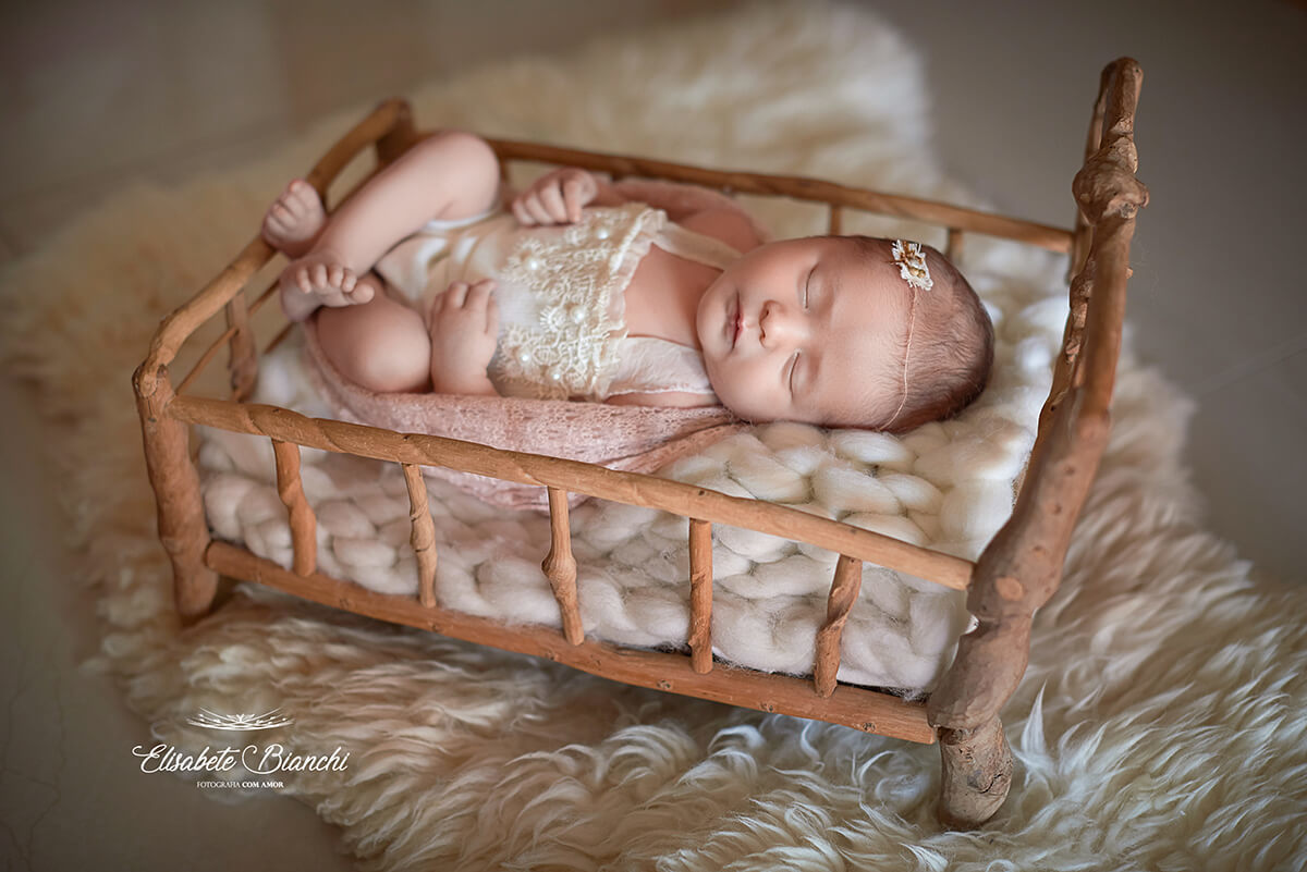 Bebê recém-nascida deitada de barriga para cima, em uma caminha de madeira rústica, em ensaio newborn, em Caxias do Sul-RS.