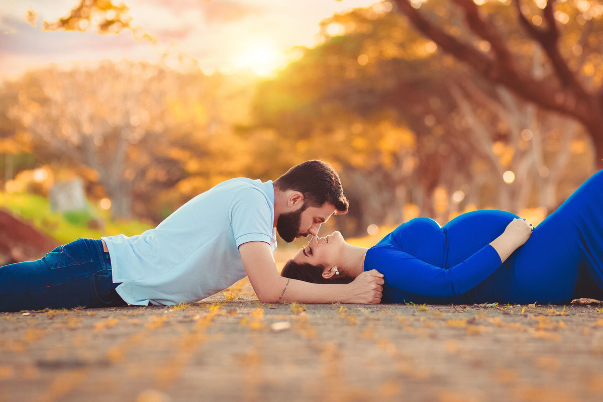 papai e gestante de vestido azul deitados  no caminho dos flamboyant, em santa bárbara d'oeste - SP
