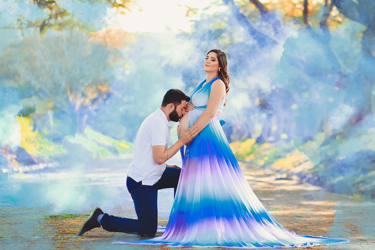 Papai ajoelhado beijando a barriga da mamãe que está com vestido arco íris, no caminho dos flamboyant, em santa bárbara d'oeste - SP