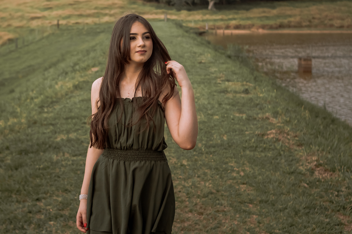 Ensaio de 15 anos em Ribeirão Preto com luz natural – Ana Júlia em meio à natureza, vestindo roupa clara, com expressão serena e olhar suave, refletindo a delicadeza e autenticidade dessa fase especial.